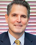 portrait of michael o'brien wearing a dark suit pale blue shirt and a gold tie