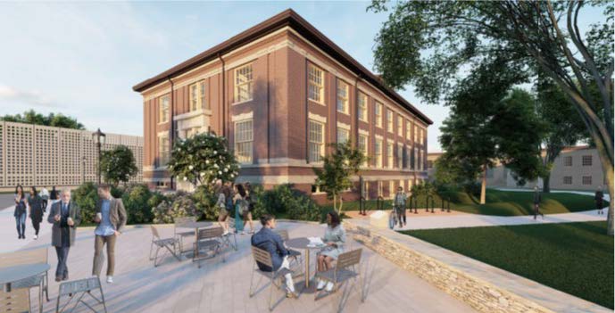 Brick two story building with large windows. 1/2 story basement viewable above ground.  patio with seating to the left of the building.  Greenery around the perimeter of the building