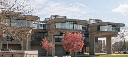 Cement building with three levels, windows and red trees in front of the building