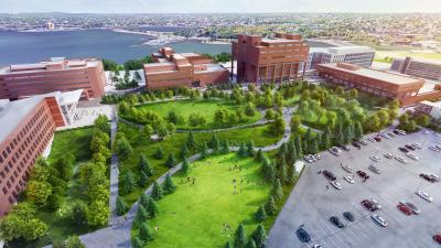 open parking lot to the right with landscape common in the middle surrounded by red brick academic buildings and water in the background