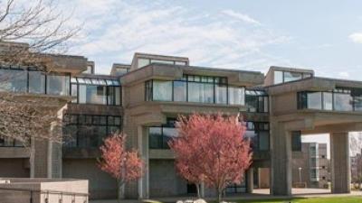 Cement building with three levels, windows and red trees in front of the building