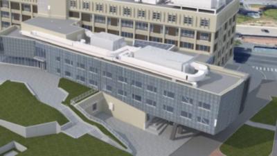 Rendering of three story building with windows and roof equipment and some grass and walkways around it. 
